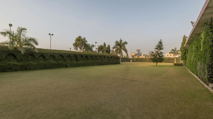 Hotel Highway Prince Paota expansive open green lawn with hedge border, palm trees, and golden hour sky in a peaceful outdoor setting.
