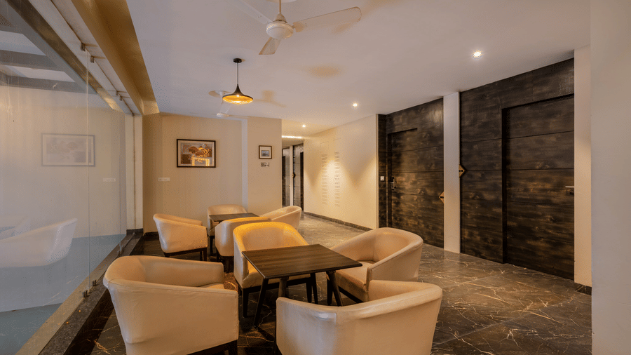 Hotel Highway Prince Paota intimate lounge with pendant lights, beige armchairs, dark stone walls, wooden doors, and polished flooring.