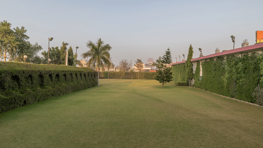 Hotel Highway Prince Paota vast open green lawn with manicured hedges, palm trees, and clear blue sky in a serene daytime setting.