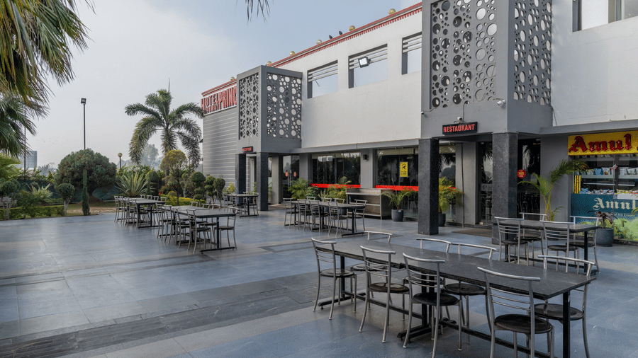 Hotel Highway Prince Paota outdoor dining terrace with black tables, chairs, decorative perforated wall, paved flooring, and daytime ambience.