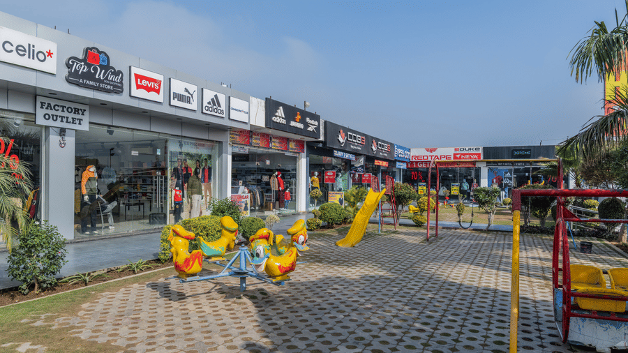 Hotel Highway Prince Paota outdoor retail plaza with commercial shops, colourful bird sculptures, open paved walkway, and dusk sky backdrop.
