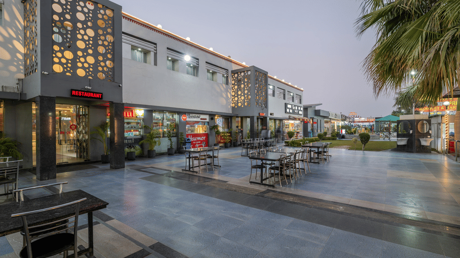 Hotel Highway Prince Paota open-air retail promenade with benches, paved walkway, lit storefronts, decorative facade, and clear evening sky.