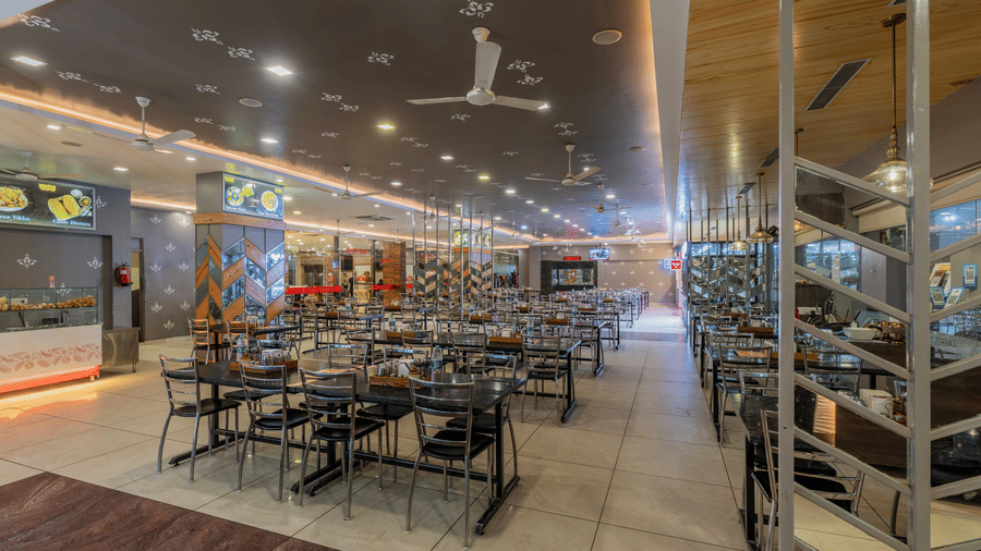 Hotel Highway Prince Paota restaurant aisle view with wooden wall panels, dark flooring, neatly set dining tables, and warm overhead lighting.