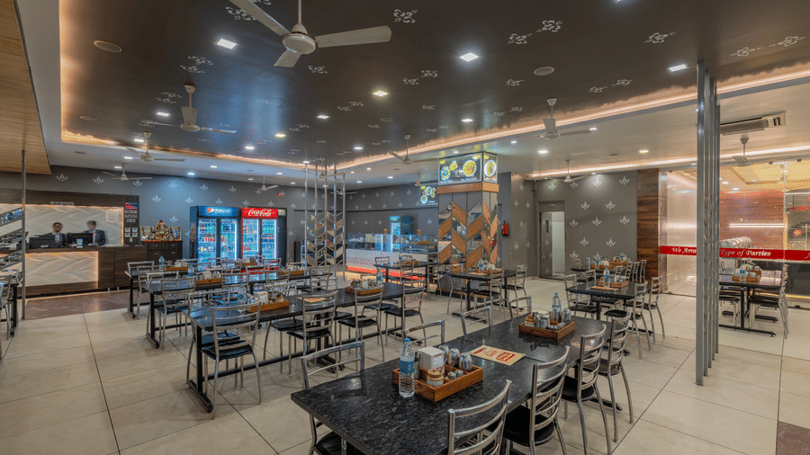 Hotel Highway Prince Paota casual dining area with dark chairs, wooden tables, warm accent lighting, ceiling fans, and vibrant wall decor.