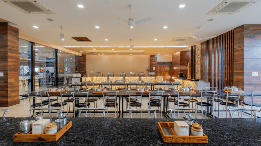 Hotel Highway Prince Paota restaurant with dark marble flooring, wooden dining tables, black chairs, warm ceiling lighting, and decorative boat display.