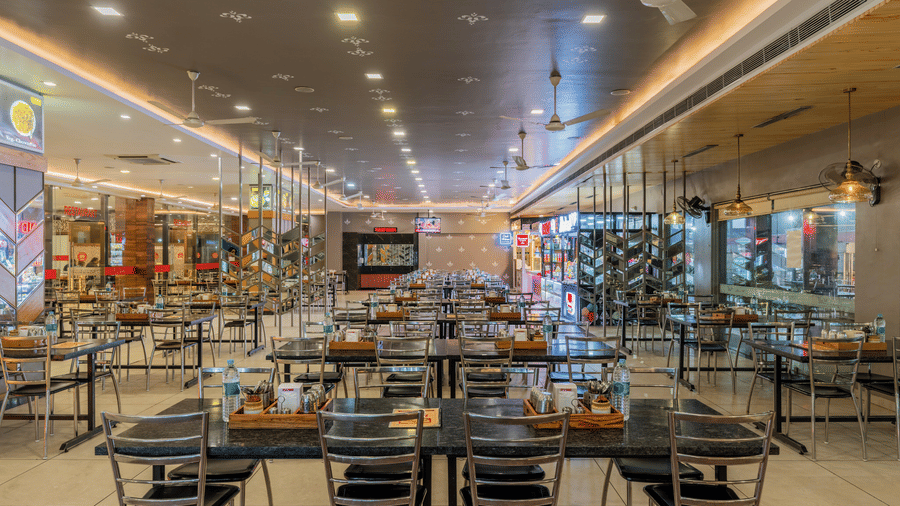 Hotel Highway Prince Paota restaurant dining hall with multiple tables, dark chairs, warm pendant lighting, and fully set dining arrangements.