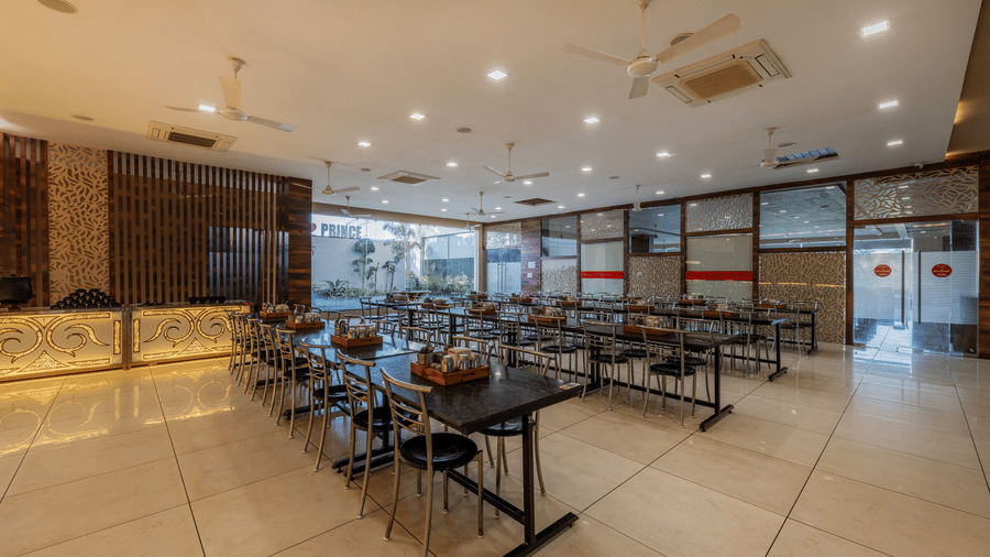 Hotel Highway Prince Paota restaurant entrance area with wooden panelled walls, dining tables, black chairs, tiled flooring, and bright lighting.
