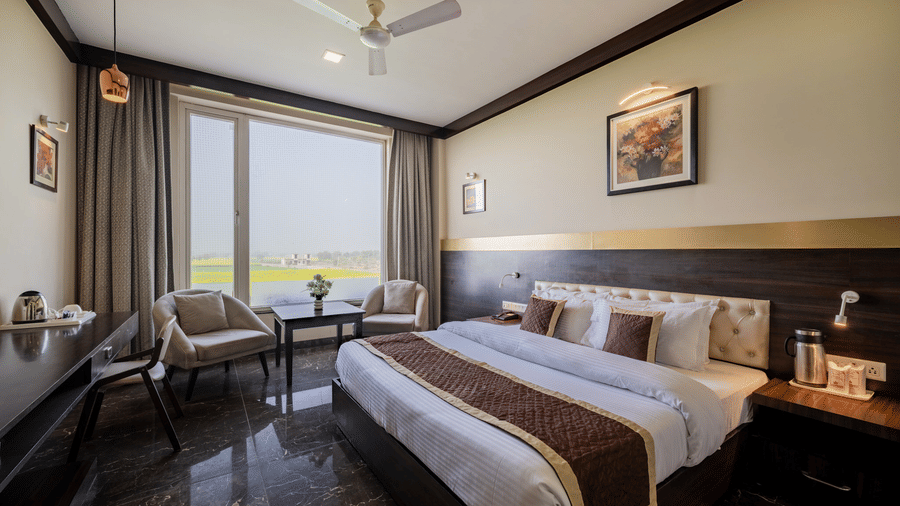 Hotel Highway Prince Paota deluxe room with two beds, brown wooden headboard, large windows, ceiling fan, and warm ambient lighting.