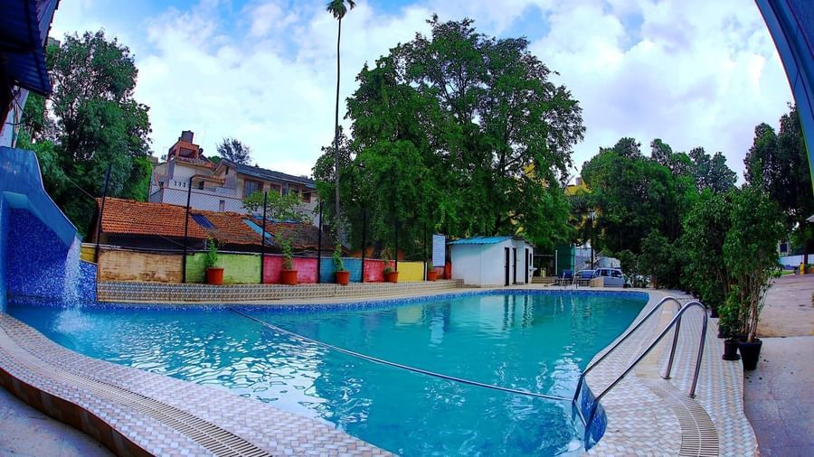 Assymetrical large swimming pool at Krushnai Resort under a partly cloudy blue sky.