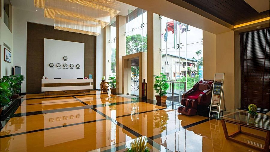 A brightly lit hotel lobby at Mansha Hotel Regency with shiny floors, a reception desk, and large glass windows looking out onto the exterior.