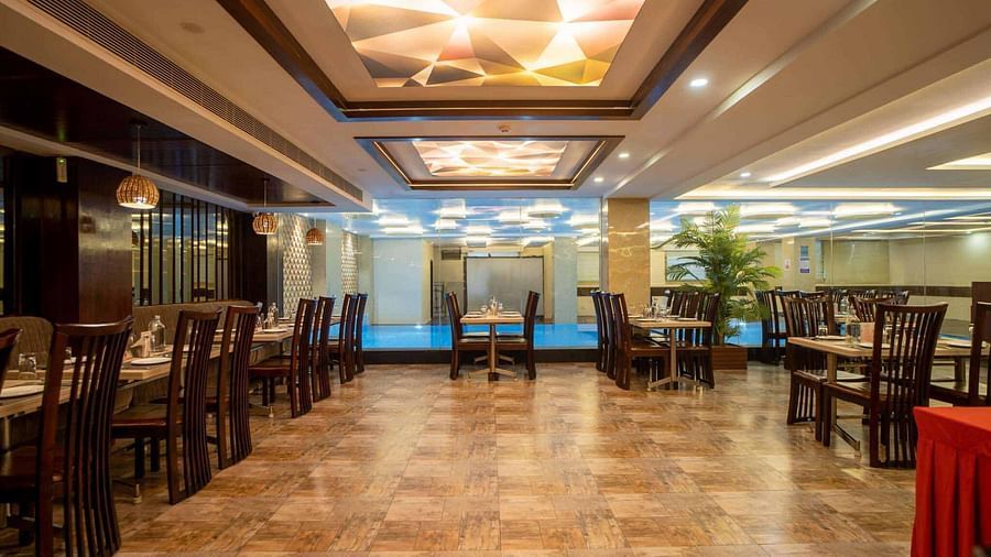 A spacious dining room at Mansha Hotel Regency with many tables and chairs, illuminated by warm lighting from the ceiling.