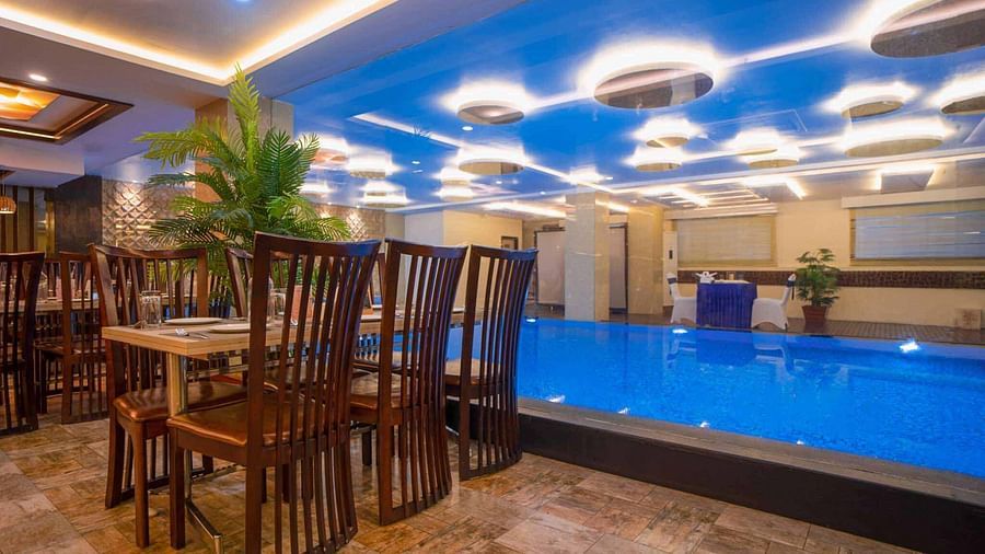 A dining area at Mansha Hotel Regency with a distinctive blue-lit ceiling, dark wooden tables and chairs, and a pool in the foreground.