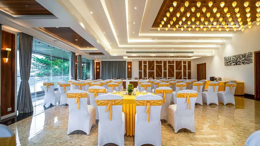 A spacious and brightly lit event hall at Mansha Palace is arranged with round tables and draped chairs.