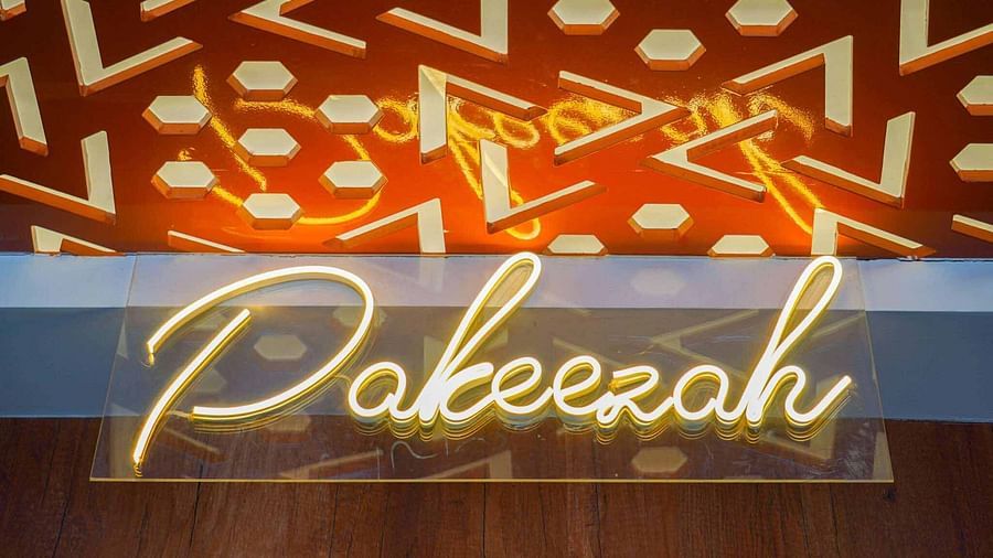 A glowing neon sign displaying Pakeezah in a cursive script is mounted on a patterned wall.