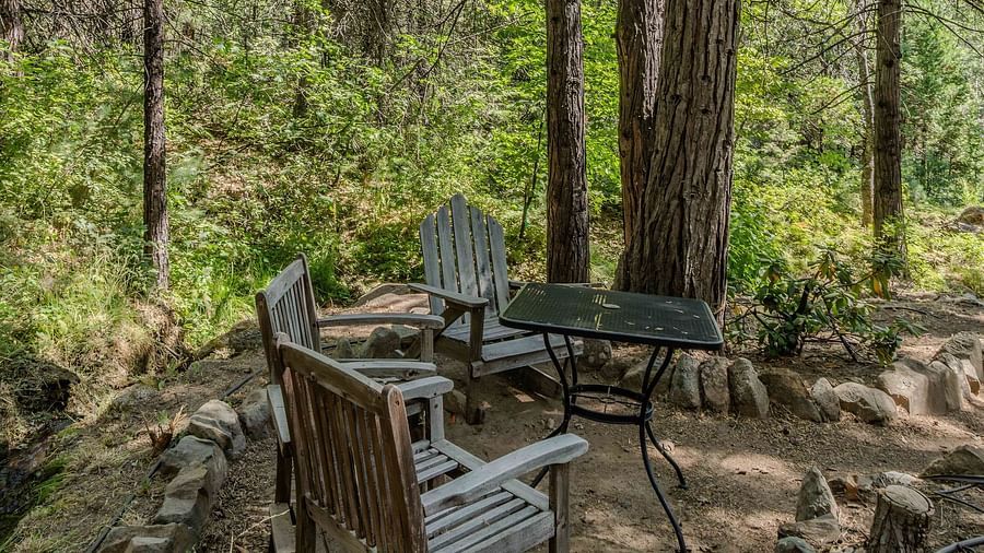 Wooden chairs and a table placed at a camp site in the forest - Narrow Gauge Inn - A Serenite Hotel Near Fish Camp.