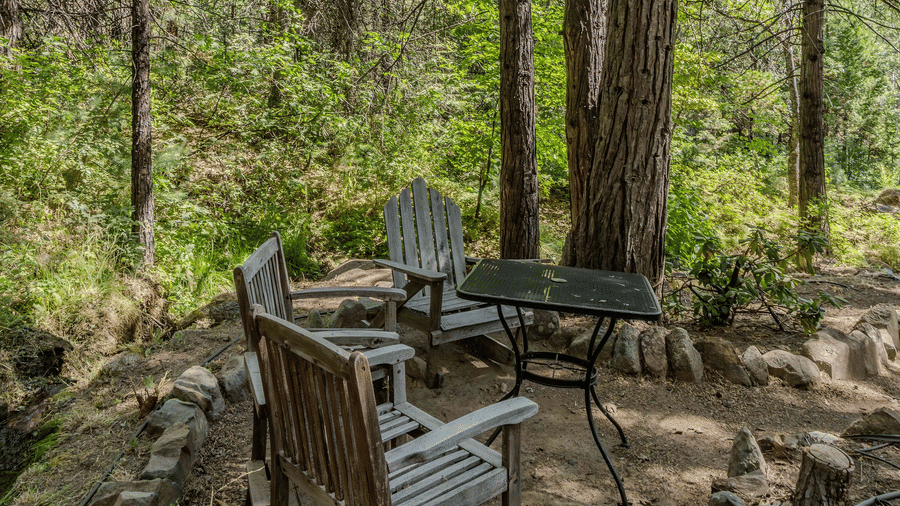 Wooden chairs and a table placed at a camp site in the forest - Narrow Gauge Inn - A Serenite Hotel Near Fish Camp.