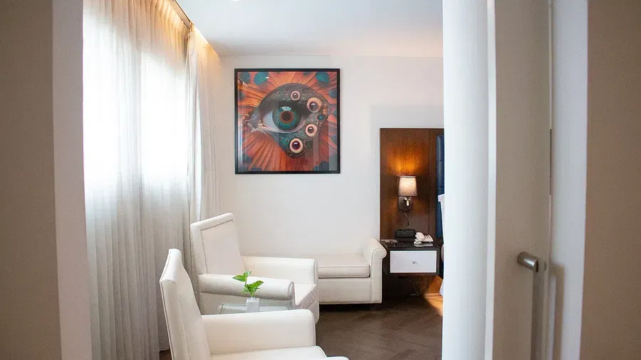 Stylish hotel seating nook with cream armchairs, colourful abstract artwork, walnut side table, and floor-to-ceiling windows with natural light at Night Hotel Bangkok.