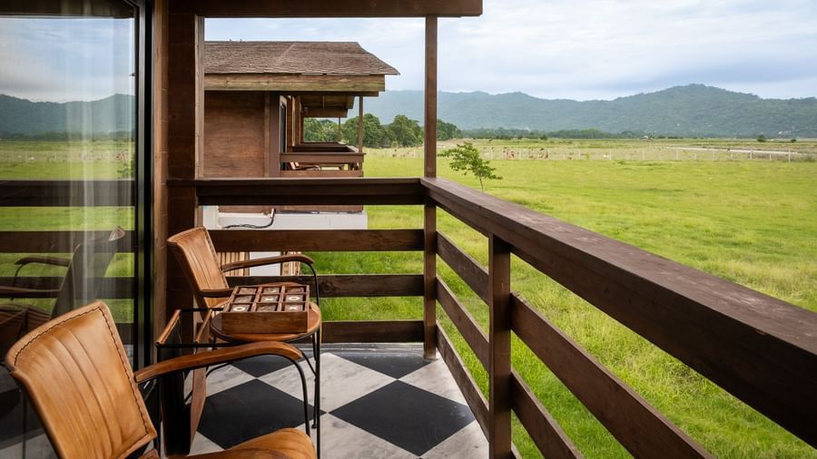 Balcony seating with wooden chairs overlooking expansive green fields and distant mountains at Rhino and River BluSalzz Collection, Pobitora.