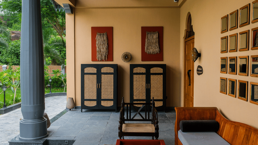 A wide-angle shot of a terrace at Rhino & River Wildlife Retreat & Spa, Pobitora, featuring stone pillars, traditional decor, and a wooden daybed overlooking the garden.