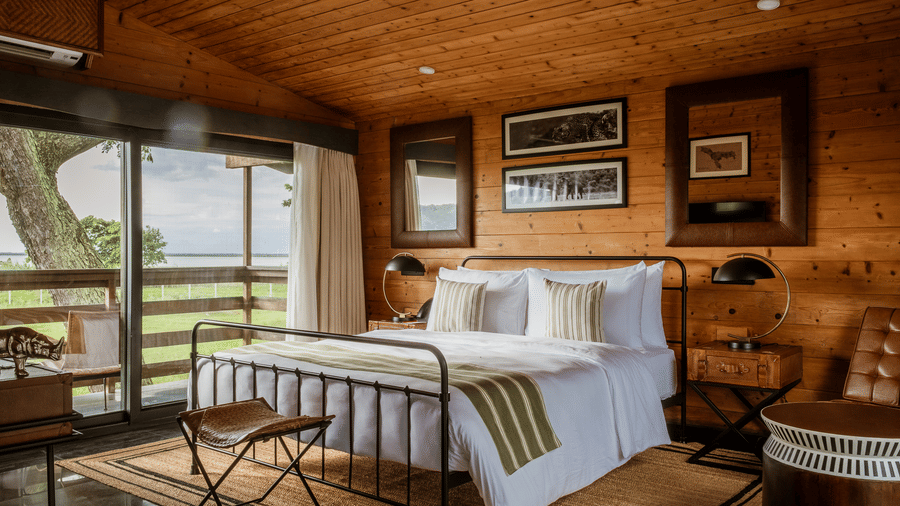 naturally lit bedroom at Rhino & River Wildlife Retreat & Spa, Pobitora, with all-wood walls, a queen size bed, and framed artwork on the wall.
