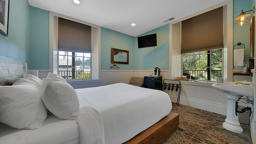 Image of a room with a double bed and a television with light blue walls and a white ceiling - The Groveland Hotel.