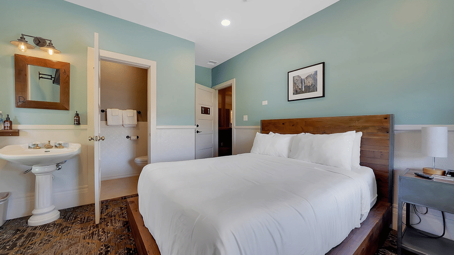 One of our rooms near Yosemite National Park, featuring sage green walls, a wooden bed with crisp white bedding, and a pedestal sink with mirror.
