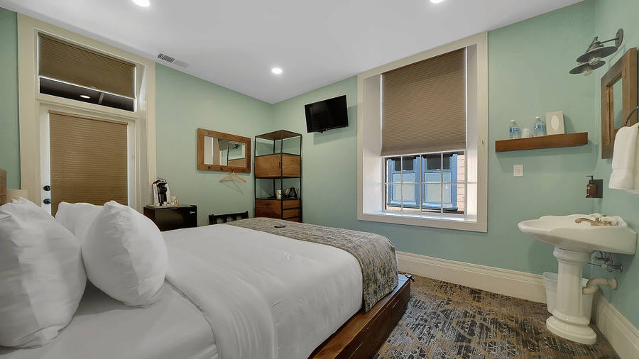 A charming lodging in Groveland at Groveland Hotel with sage green walls, wooden platform bed, pedestal sink, and patterned area rug throughout.