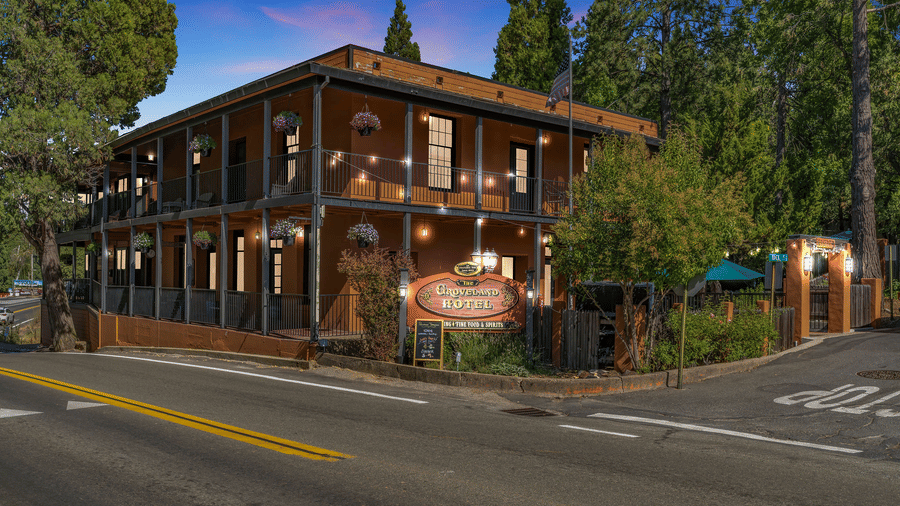 Facade of The Groveland Hotel with trees surrounding the building on a clear, blue day.