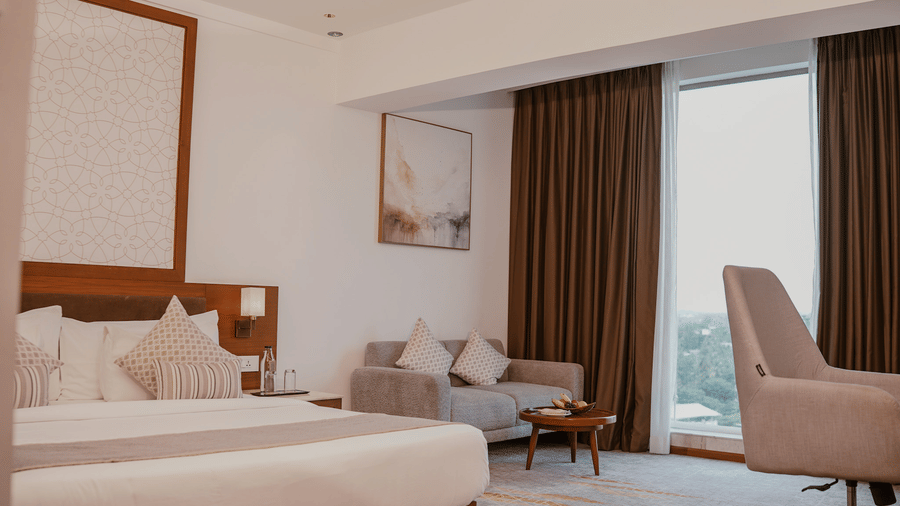A bedroom features a king size bed, a grey 2 seater sofa, and a grey desk chair near a window at Tiara by MPS.