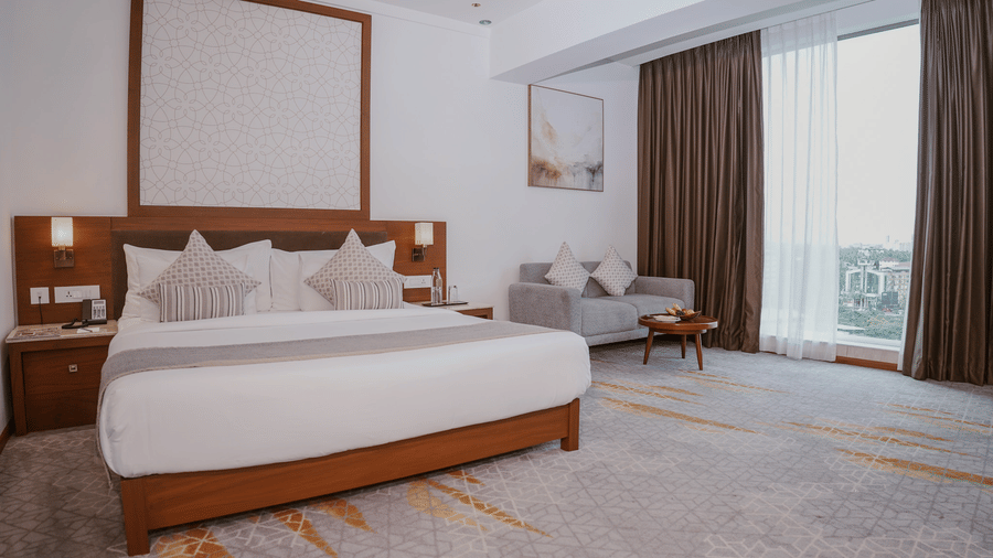 A spacious bedroom features a king size bed, a grey 2 seater sofa, and a tall glass window at Tiara by MPS.