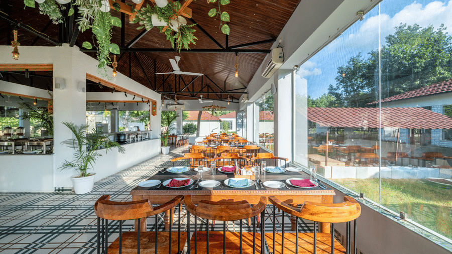 Dining area beside a full-height glass wall at Valley by Grassfield, a resort in Jaipur.