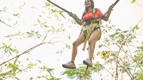 Person mid-air on a zip line adventure, surrounded by lush green trees.