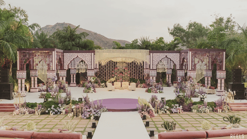 Grand outdoor wedding mandap setup with a mountain backdrop, floral aisle, and symmetrical seating.