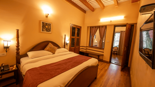 Elegant bedroom at The Pavilion, Nainital featuring wooden four-poster bed with red runner, exposed beam ceiling, and traditional furnishings.