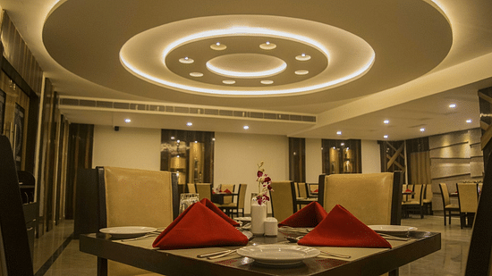 A close-up view of a table-chair set, set against a ceiling adorned with circular designs - Wedlock Greens Hotel Resorts Dhanbad