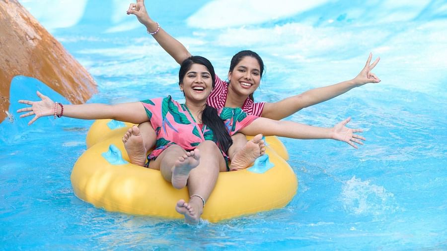 Two women smiling on a yellow inflatable float in a pool, arms raised in excitement.