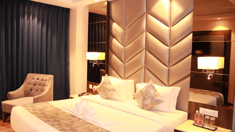 The premier room of Sarovar Portico, Somnath, with a double bed and a lone chair by the window