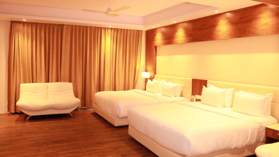 A warmly-lit bedroom with 2 double bed and a twin seating sofa by the window at the Family suite of Sarovar Portico, Somnath