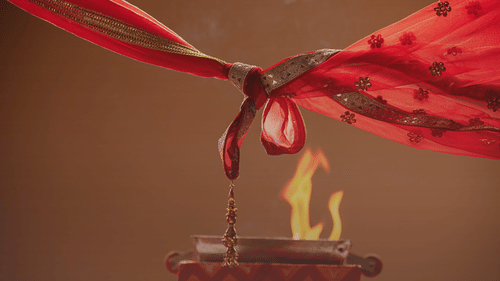 A knot tied by two design fabric pieces above the fire implicating a wedding ceremony that is taking place.