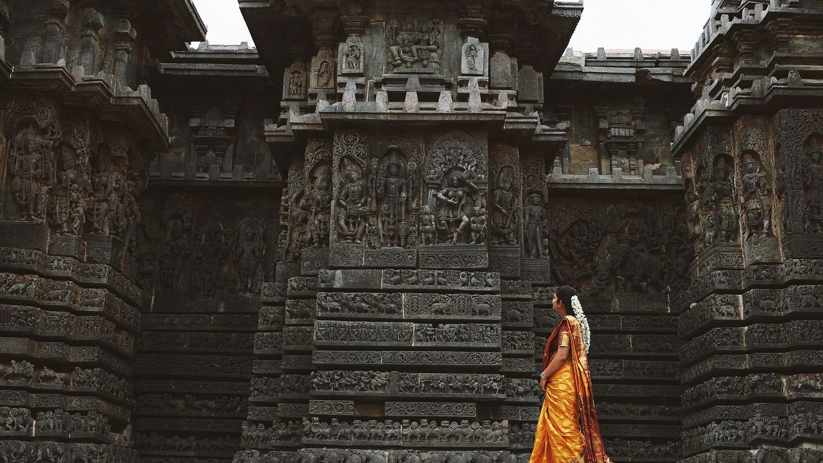 image of a woman dressed in a yellow saree walking in front of a temple
