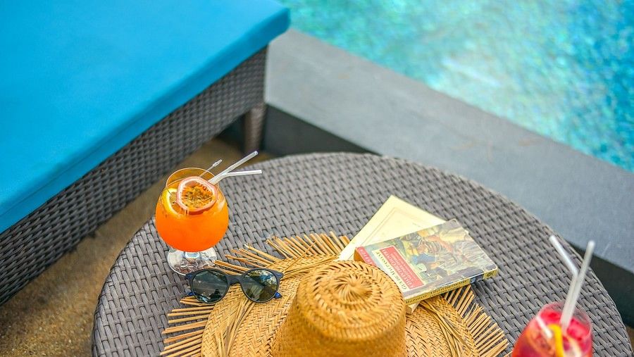 image of the table on the poolside with refreshing drinks, a straw hat, sunglasses and a book - Maikhao Dream Villa Resort & Spa, Phuket