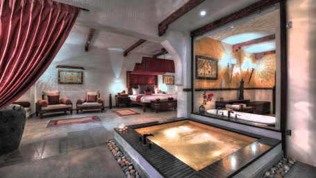 A spacious interior featuring a sunken stone bathtub and red velvet curtains overlooking a private garden at Earthitects.