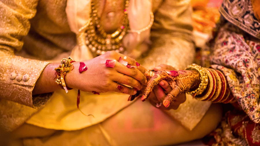 Traditional Indian wedding ceremony with groom placing a ring on bride’s mehndi-adorned hand surrounded by rose petals.