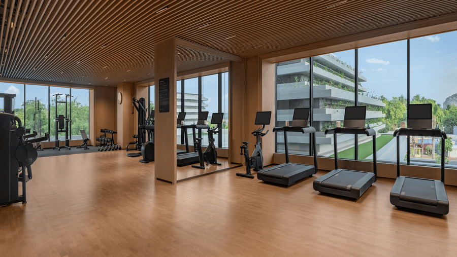 Gym with treadmills and cardio equipment set against large windows with a city view at The Residency Signature Madurai.