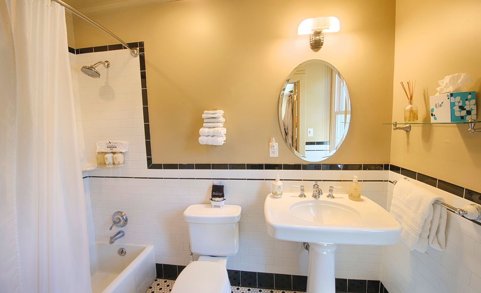 a bathroom highlighting a wash basin with an oval shaped mirror along with a commode and a bathtub besides it - Historic Tapoco Lodge
