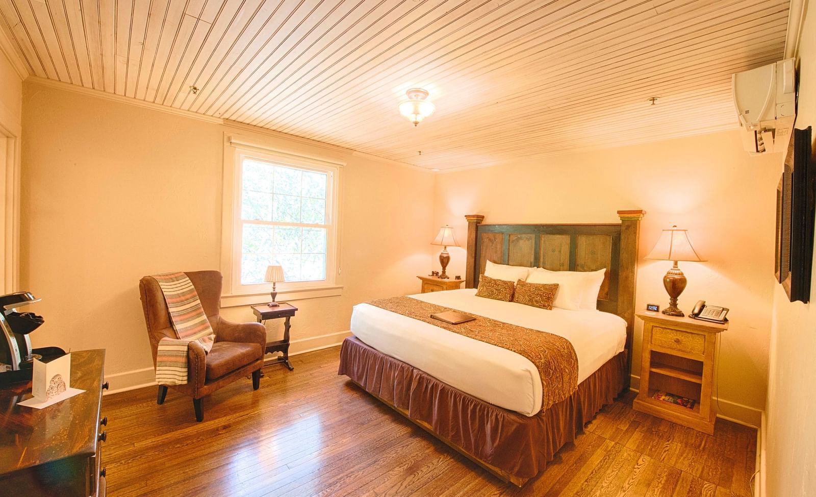 full view image of a brightly lit bedroom with a comfortable double bed with a heady headboard along with an armchair - Historic Tapoco Lodge