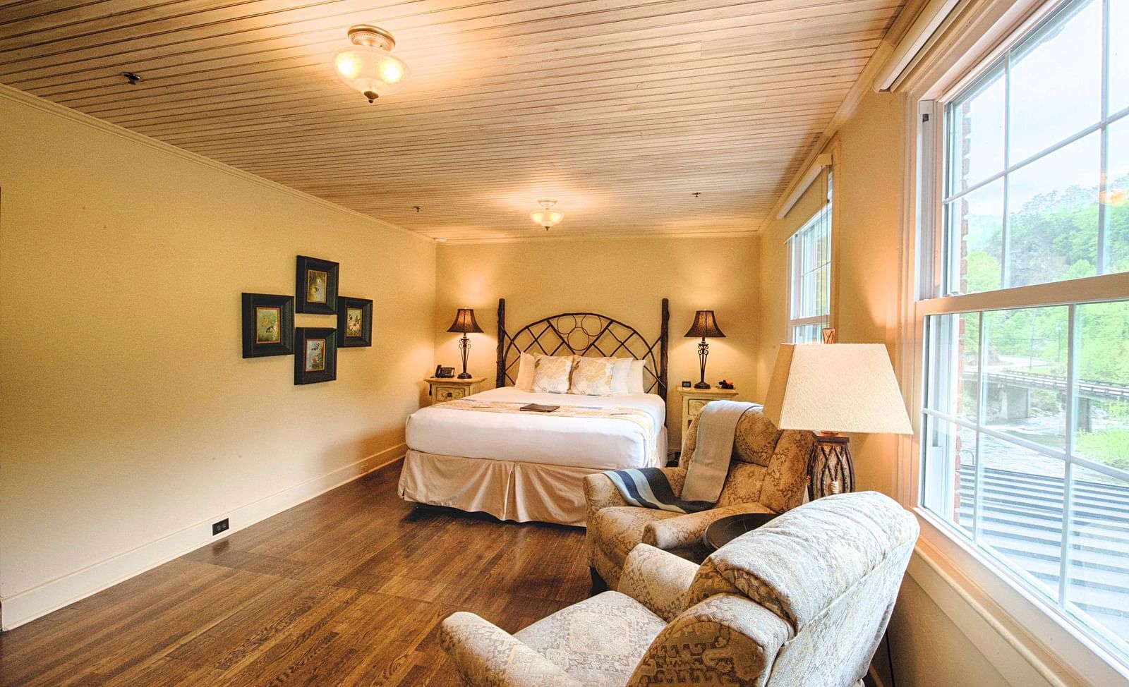 a room with wooden flooring and cream colored walls featuring a double bed in the middle of the room along with a seating area - Historic Tapoco Lodge