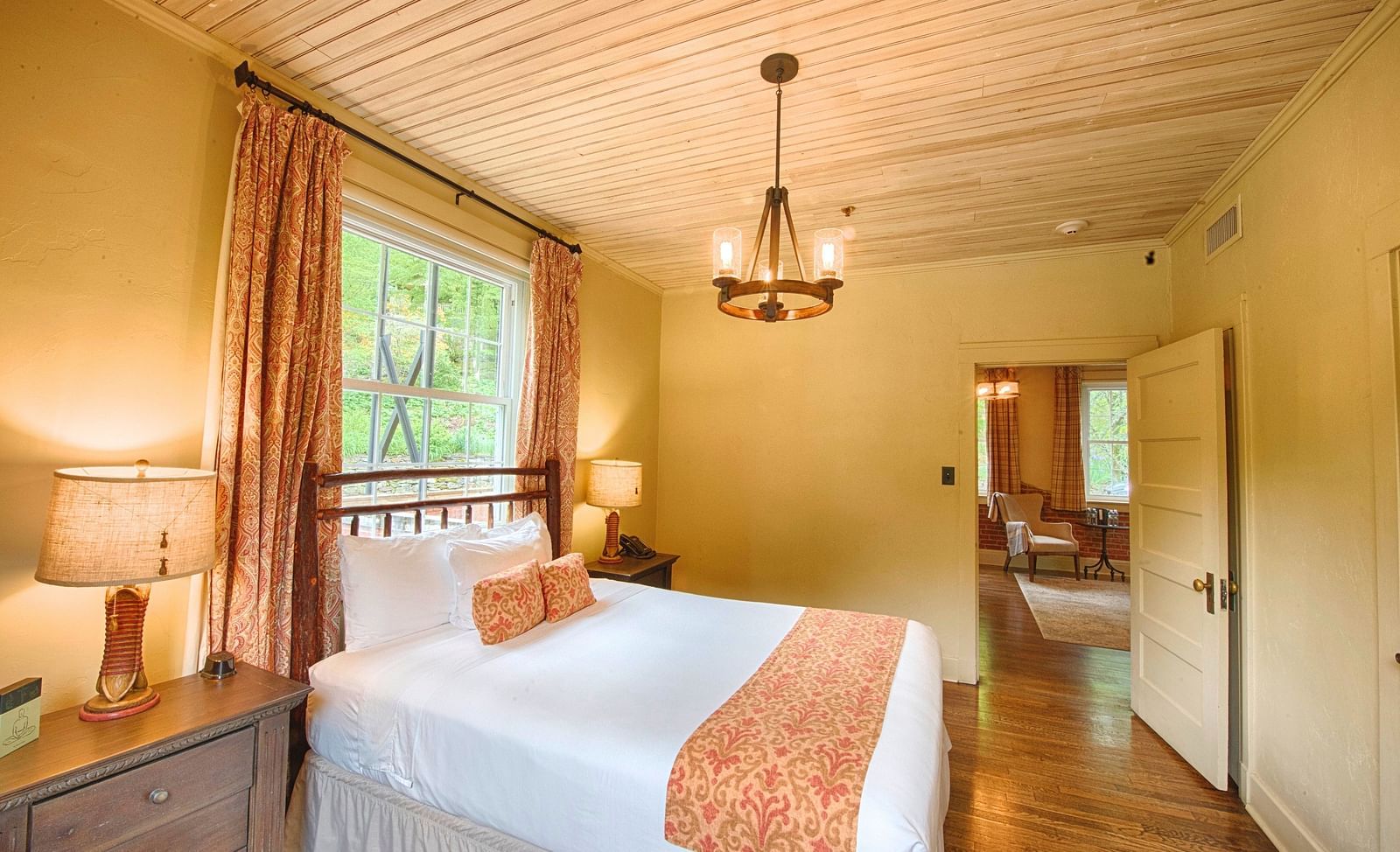side view image of a double bed right under the chandelier with a window behind the bed - Historic Tapoco Lodge