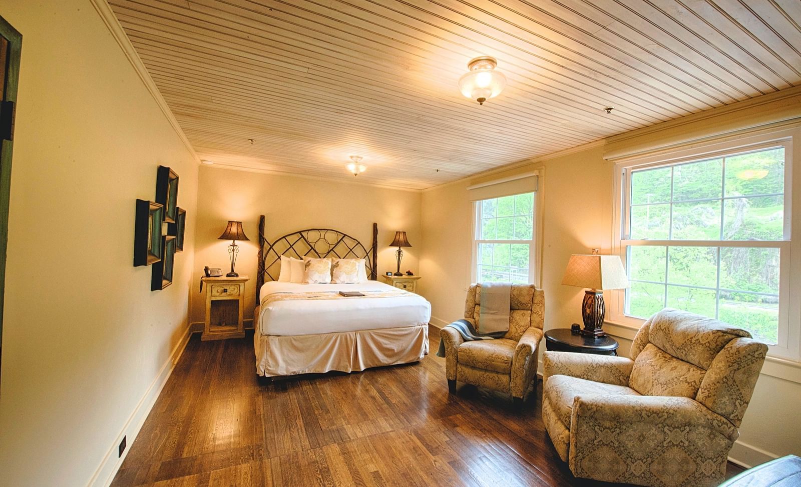 full view image of a room with wide windows featuring a cozy double bed and comfortable cushioned armchairs in front of it - Historic Tapoco Lodge