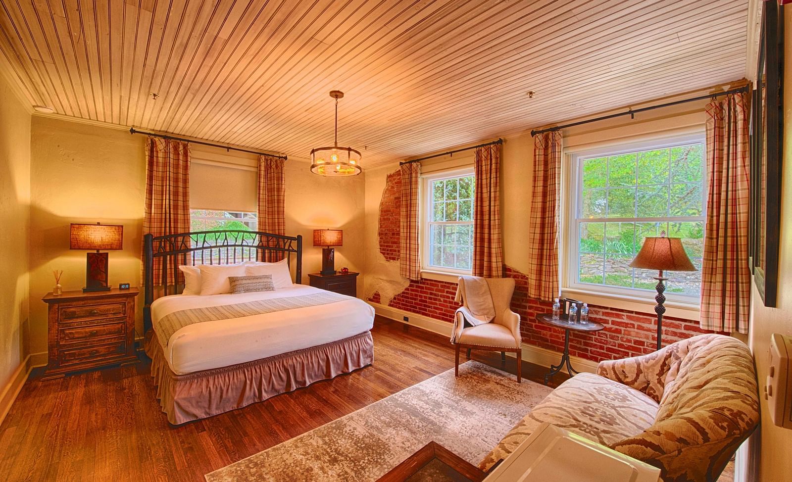a room with ample natural lighting coming from the huge windows in the room with plush arm chairsa brightly lit bathroom featuring a door opening to the bedroom overlooking the double bed - Historic Tapoco Lodge